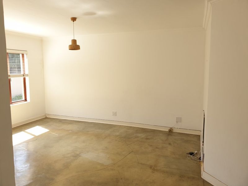 A bright, empty bedroom featuring polished concrete floors, neutral walls, and a window with fitted blinds, offering a clean canvas for personalization.