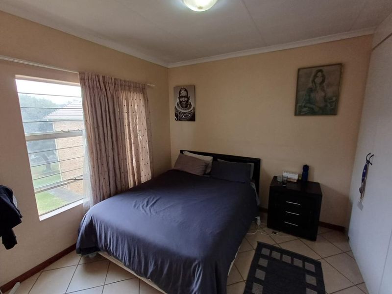 A functional bedroom featuring tiled flooring, a built-in wardrobe, and a louvered window providing natural light.