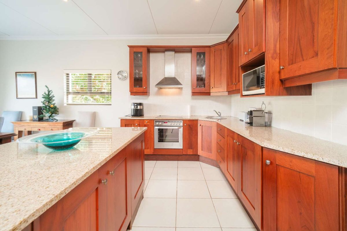 A well-maintained kitchen featuring warm-toned wooden cabinetry, granite countertops, a central island, and integrated stainless steel appliances including an oven and extractor fan.