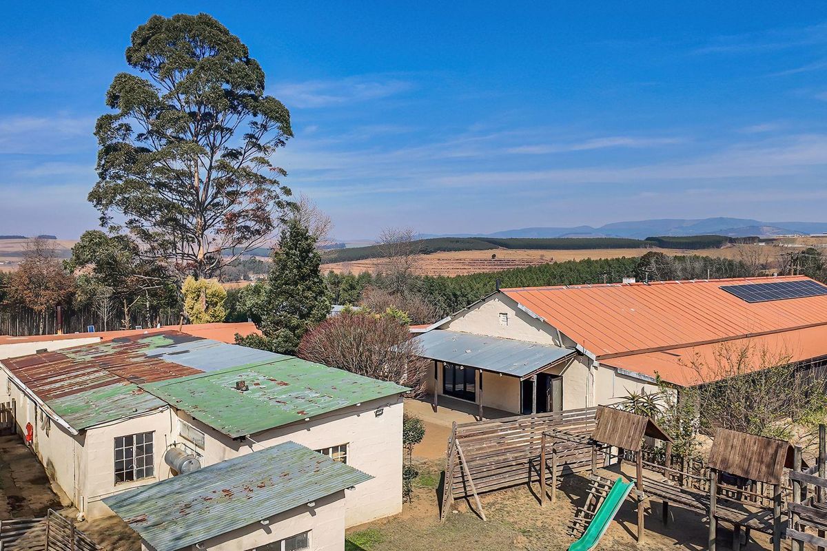 Aerial view of the small holding property featuring multiple outbuildings with corrugated metal roofs, solar panels, and an outdoor timber play area.