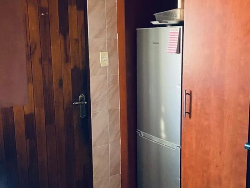 A functional kitchen area featuring built-in wooden cabinetry, tiled flooring, and a tiled wall splashback with decorative ceiling detailing.