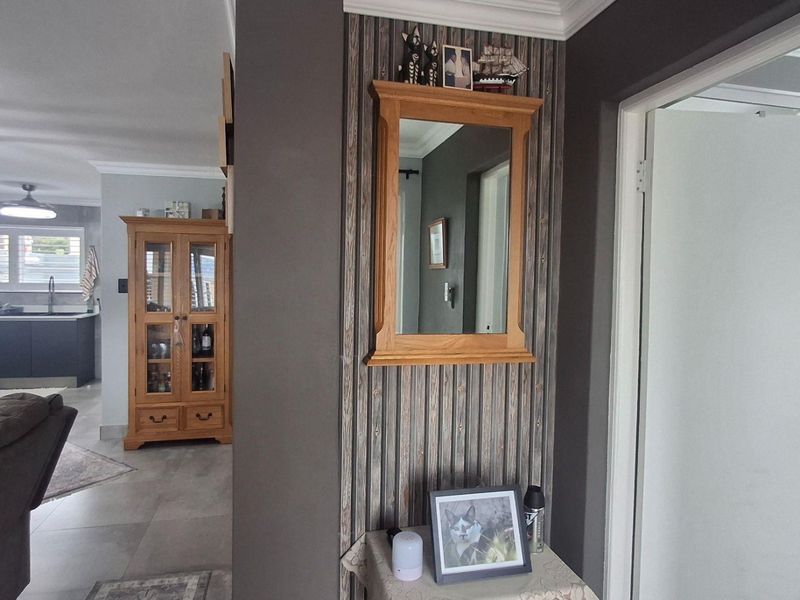 An open-plan living area featuring a modern kitchen with island, neutral tiled flooring, and coved ceilings, connecting seamlessly to the hallway entrance.