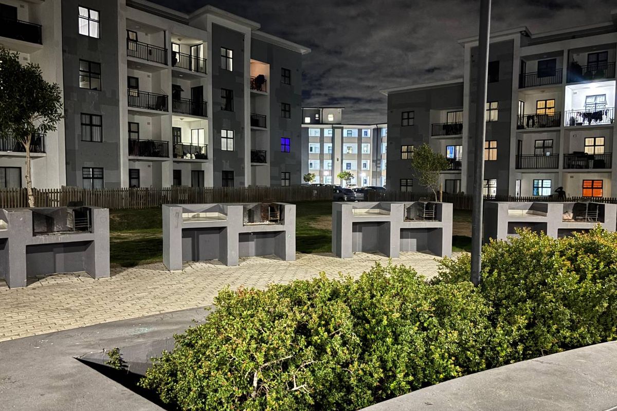 Communal outdoor area featuring multiple built-in brick braai stations set within a landscaped complex, illuminated for evening use.