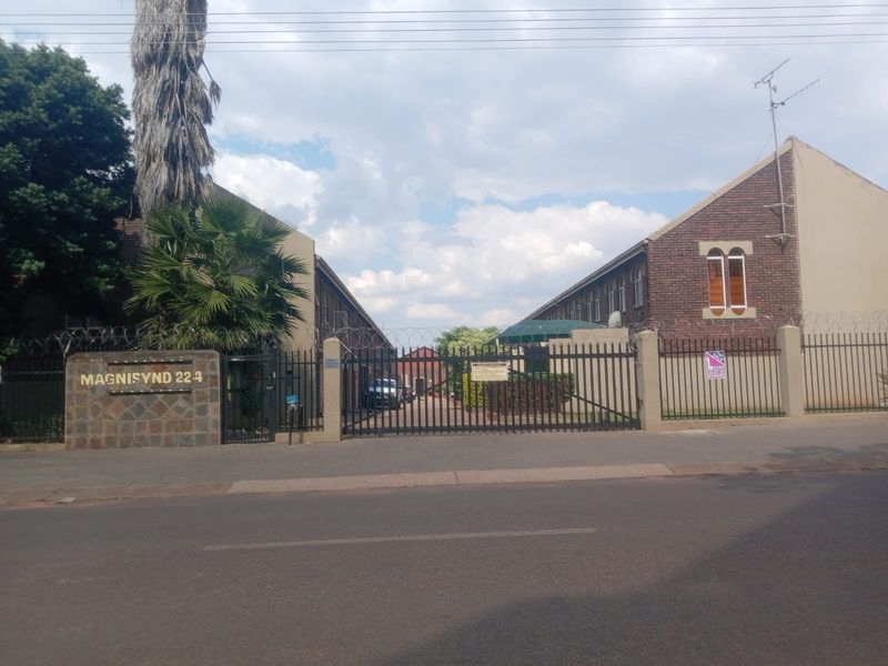 Street view of the Magnisynd 224 apartment complex entrance, featuring secure gated access, brick building facades, and perimeter security fencing.