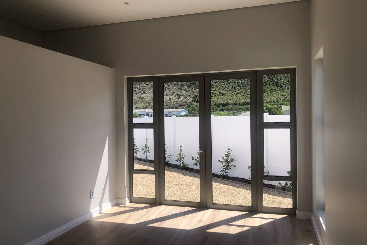 A bright, empty living room featuring modern wood-look flooring and large aluminium-framed glass doors opening to a private rear garden.