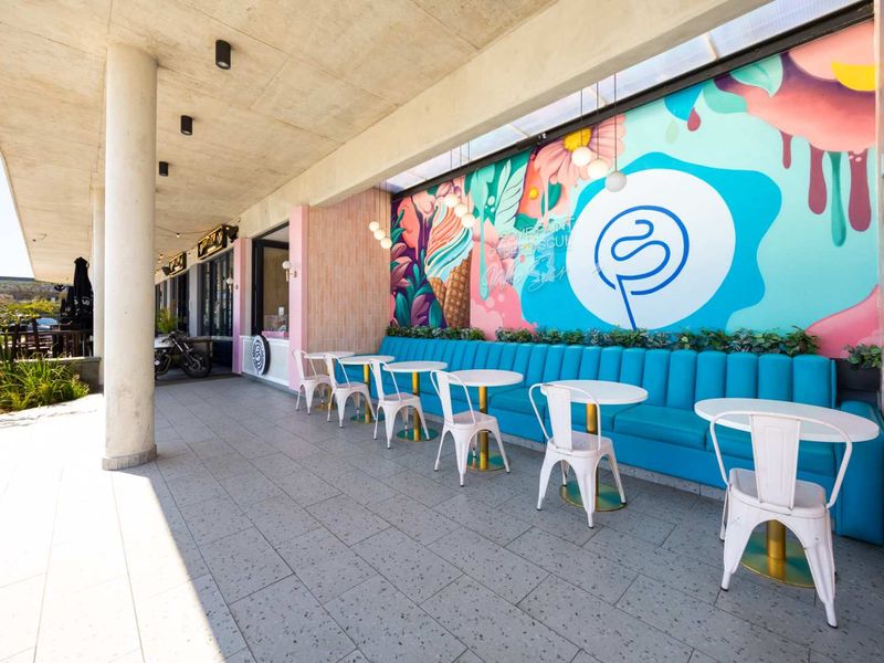 A vibrant outdoor patio area featuring a large colorful mural, built-in bench seating, and modern tiled flooring under a covered concrete ceiling.