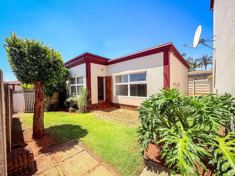 Rear view of the townhouse featuring a private garden, paved patio area, and established lawn with boundary walling.