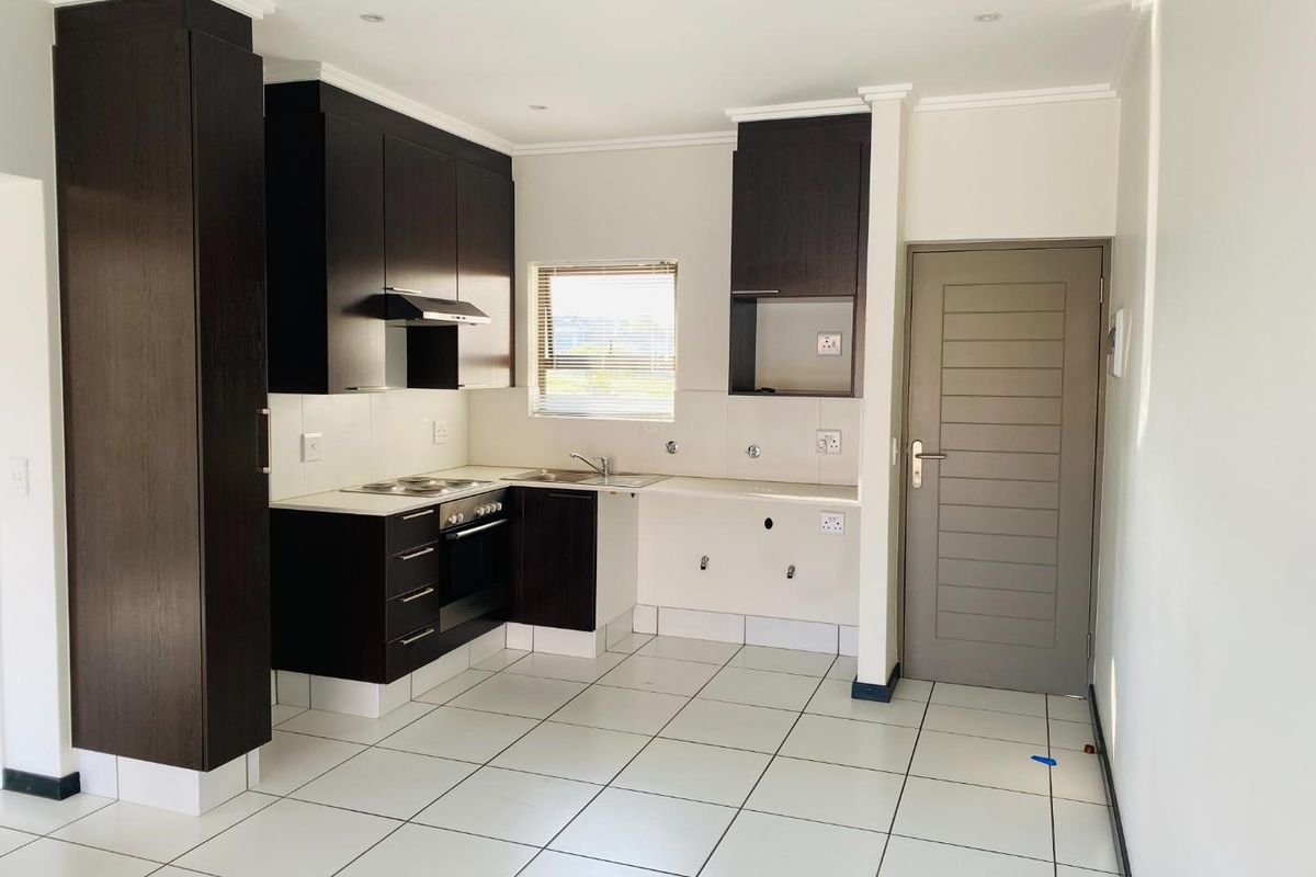 A clean, modern kitchen featuring dark wood cabinetry, built-in oven and hob, tiled flooring, and a neutral backsplash, ready for appliance installation.