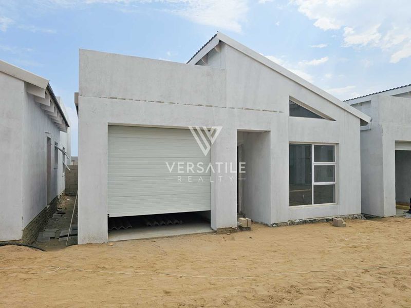 Front elevation of a modern townhouse featuring a single garage, aluminium window frames, and a pitched roof, currently in the final stages of construction.