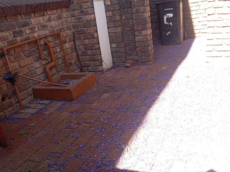 A rear courtyard area featuring exposed brick walls, paved flooring, and external plumbing fixtures with a concrete wash basin.