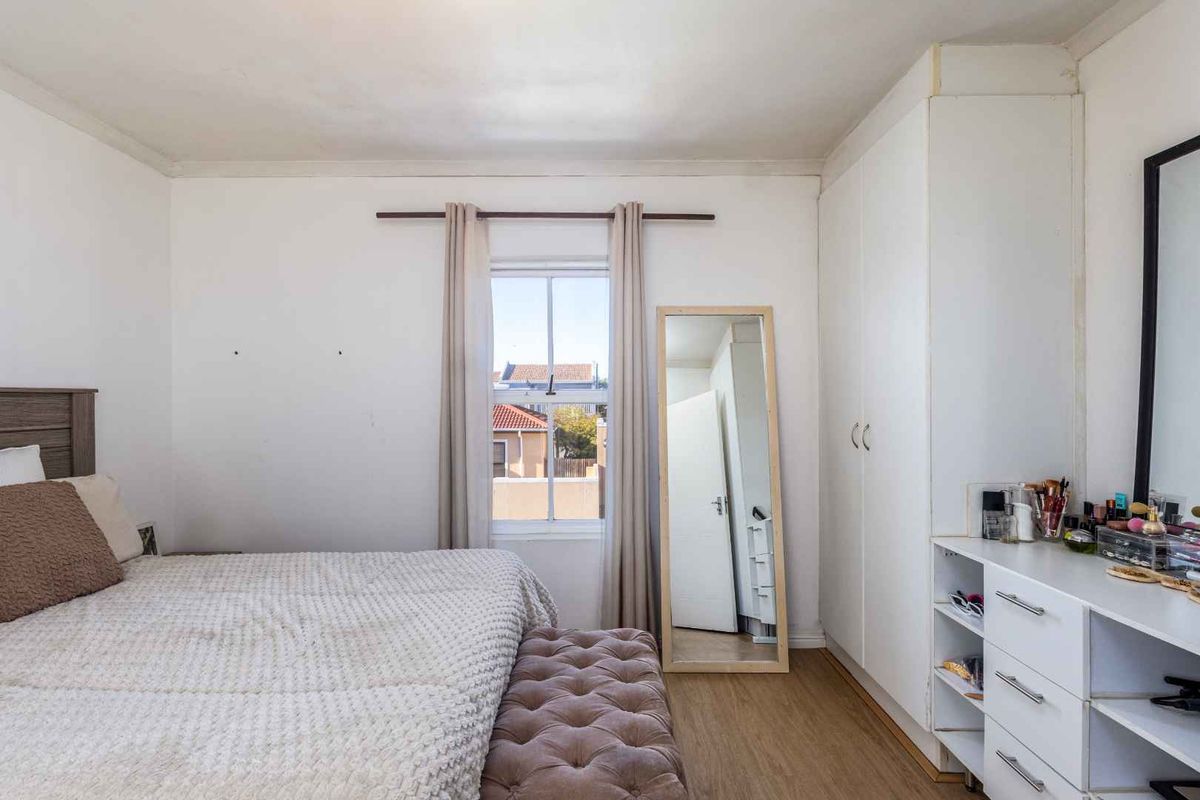 A bedroom featuring built-in cupboards, laminate flooring, and a window providing natural light and a view of the surrounding neighborhood.