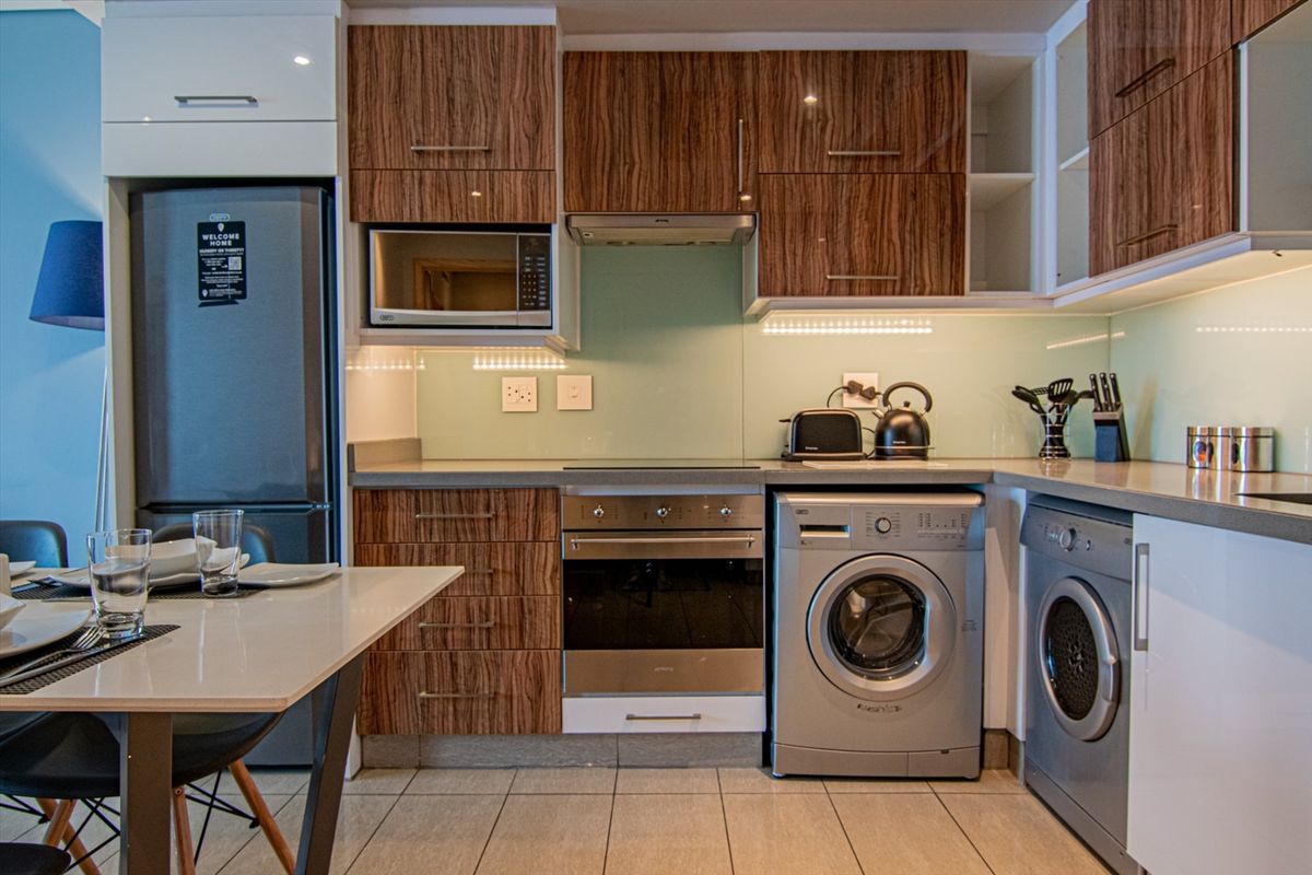 Modern kitchen featuring wood-grain cabinetry, stone countertops, integrated oven, hob, extractor fan, and built-in microwave with tiled flooring.