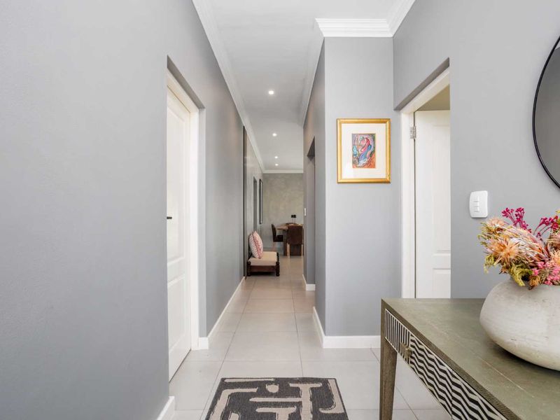 A well-maintained hallway featuring neutral grey walls, tiled flooring, recessed downlighting, and classic cornicing, leading towards the main living area.