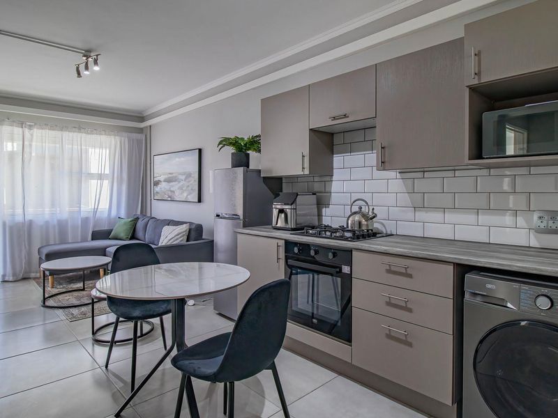 Modern open-plan living area featuring a well-appointed kitchen with subway tile backsplash, built-in appliances, and sleek cabinetry, flowing into a bright lounge space.