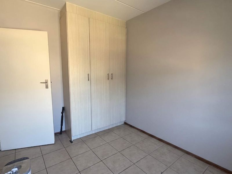 A clean, empty bedroom featuring neutral wall tones, tiled flooring, and a functional built-in wardrobe for storage.