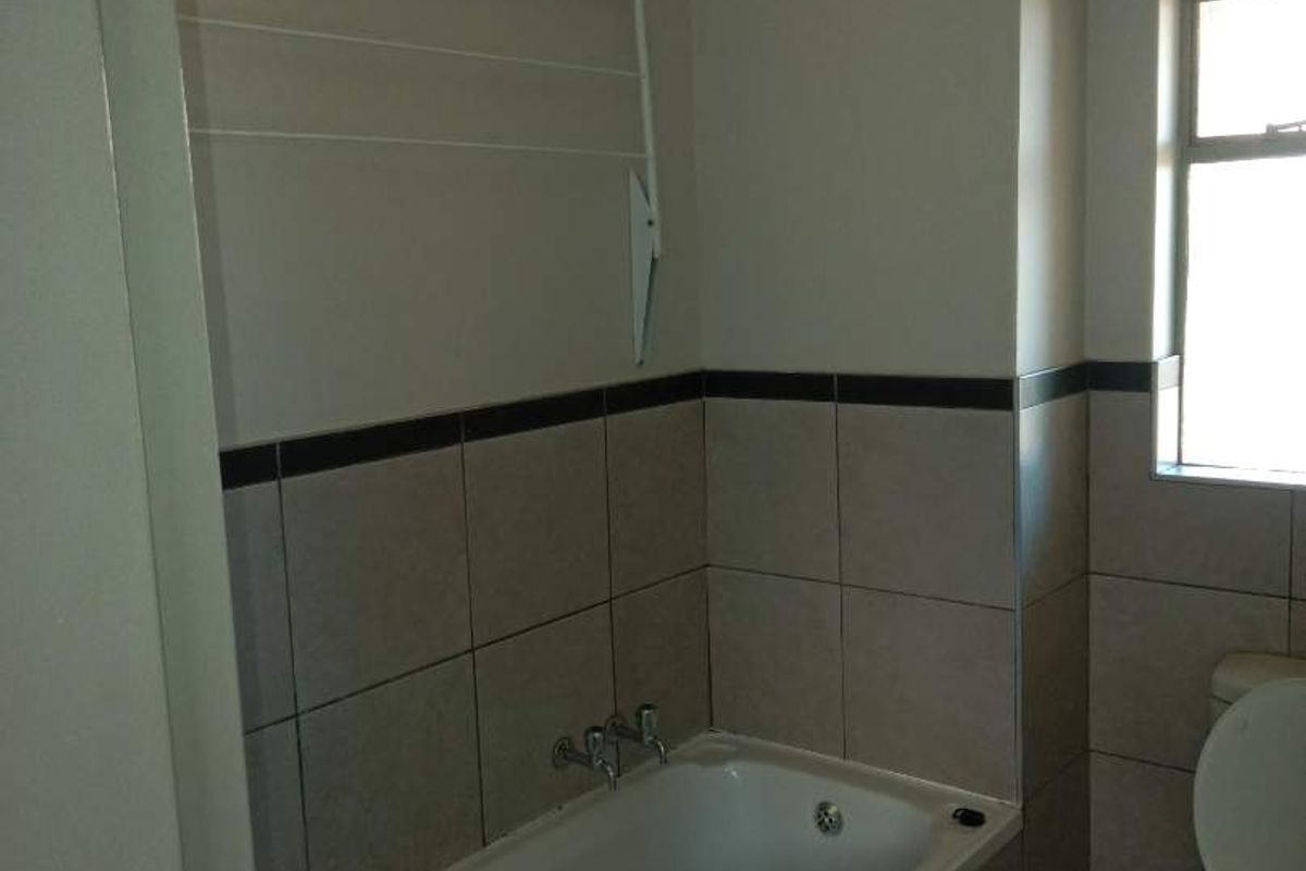 A functional bathroom featuring a built-in bathtub with wall-mounted taps, a toilet, and neutral wall tiling with a decorative border.