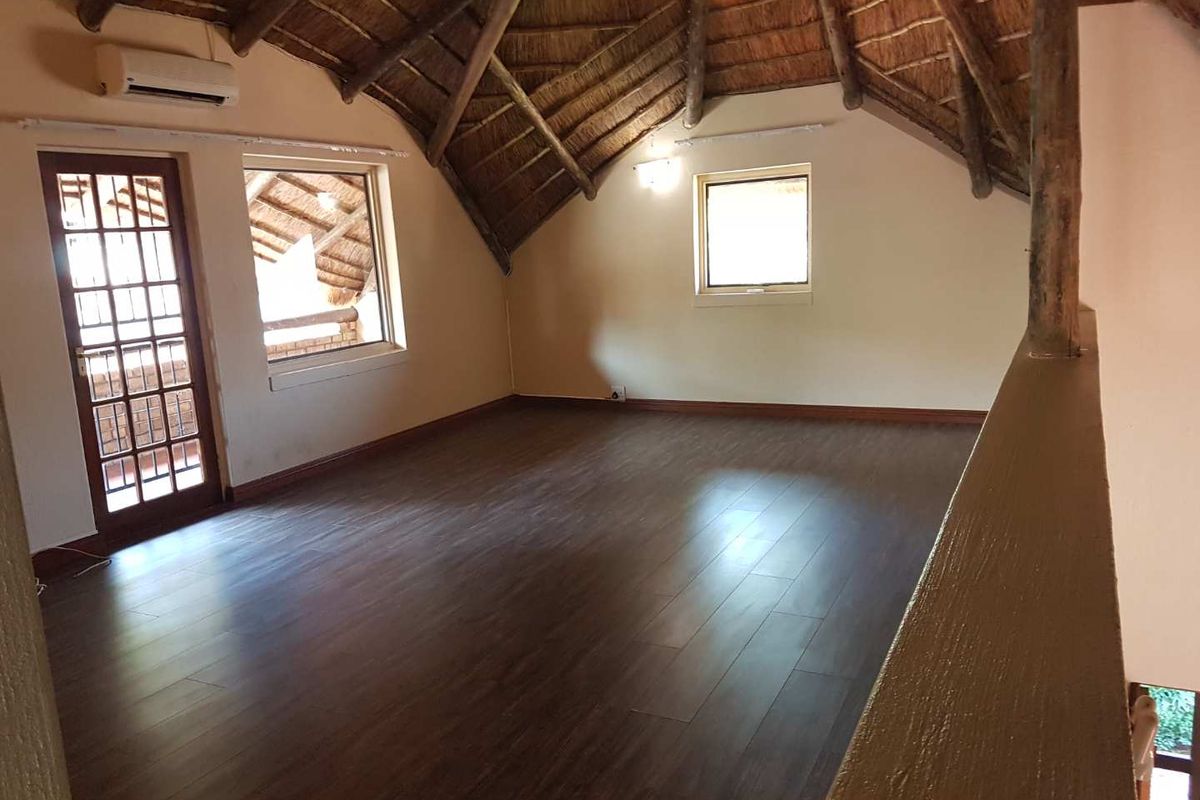Spacious loft area featuring a high vaulted thatched ceiling, dark wood-look flooring, and a private balcony access door.