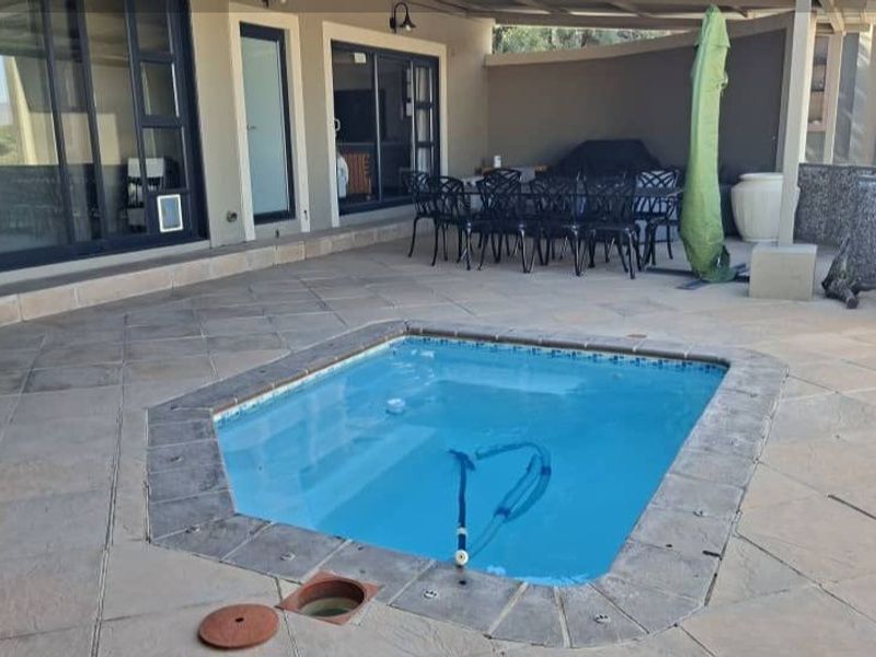 A paved outdoor patio area featuring a built-in swimming pool and direct access to the home through large sliding glass doors.
