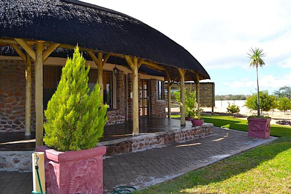 A well-maintained guest house exterior featuring a traditional thatched roof, stone-clad walls, and a spacious covered patio area overlooking the garden.