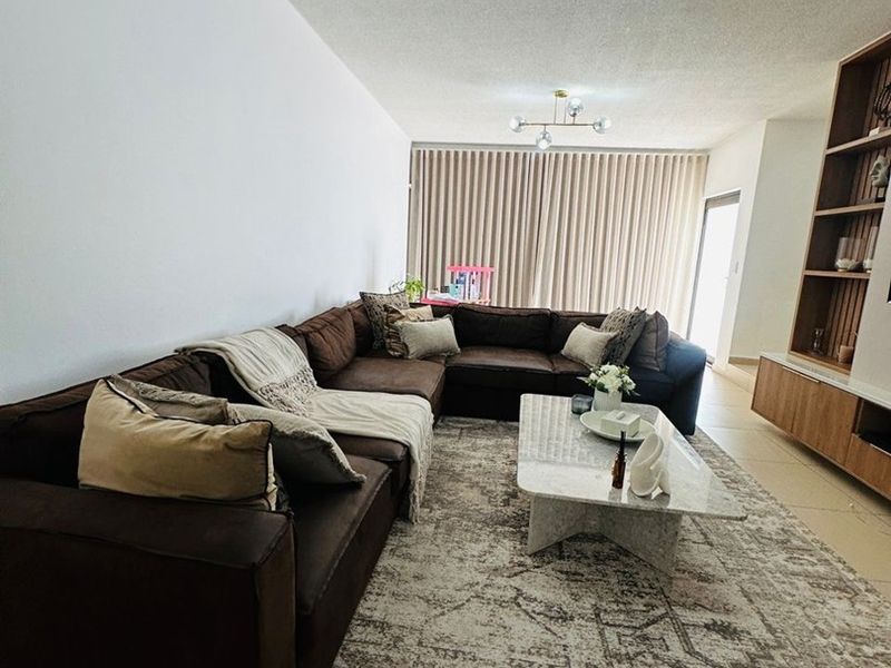 Spacious living room featuring tiled flooring, a custom built-in shelving unit, and modern lighting, creating a comfortable and functional living space.