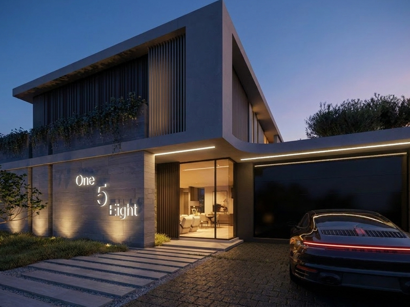 A contemporary architectural front elevation featuring stone cladding, integrated facade lighting, a paved driveway, and a sleek garage entrance.