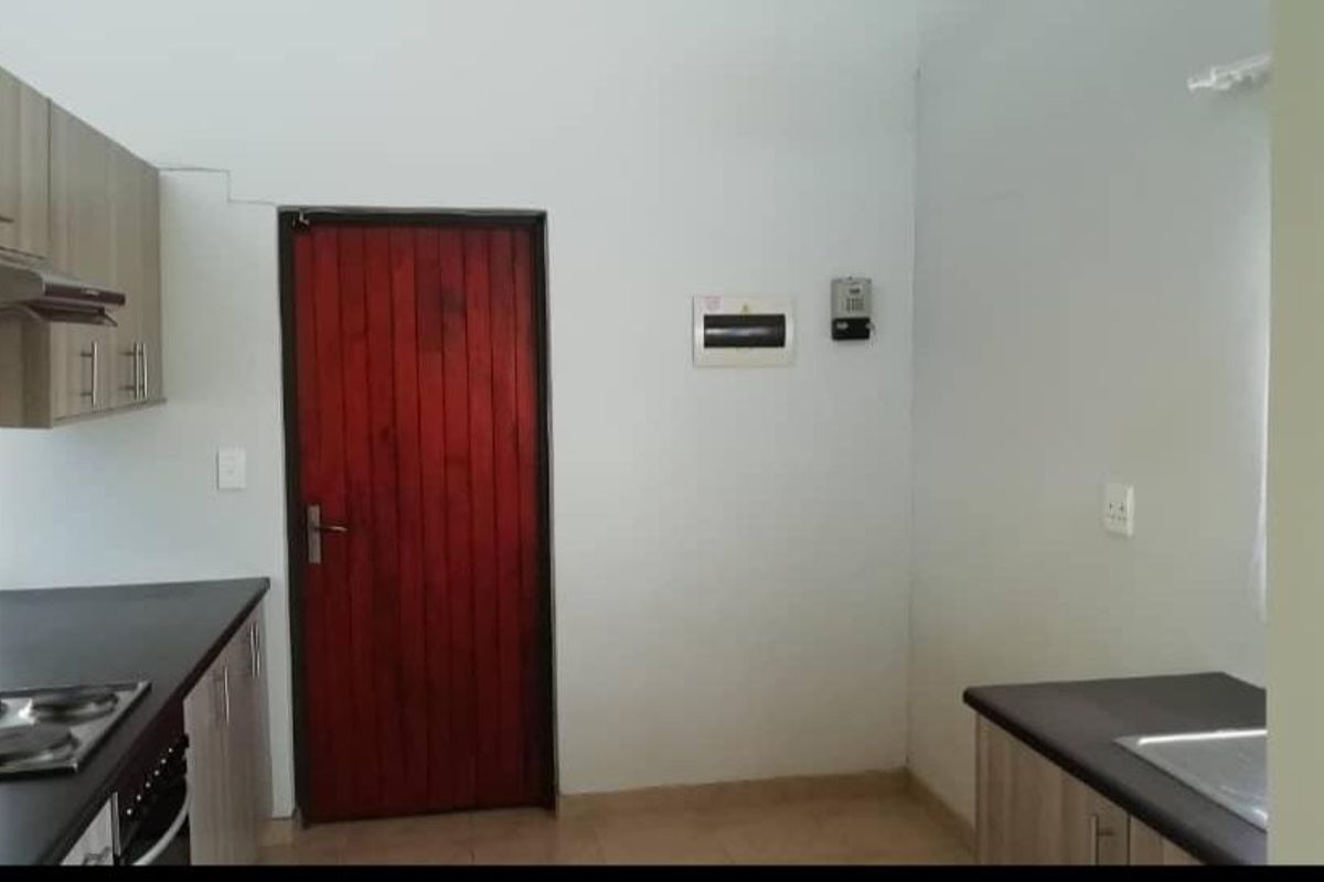 A functional kitchen area featuring wood-look cabinetry, dark countertops, a built-in electric hob, and a red wooden door.
