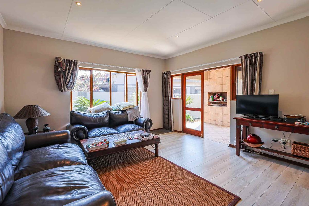 A spacious living room featuring light-toned laminate flooring, recessed ceiling lighting, and direct access to an outdoor patio area through a wooden door.