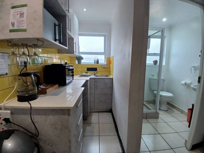 Compact kitchen area featuring modern grey cabinetry and yellow tiled backsplash, adjacent to a small bathroom with a shower and toilet.