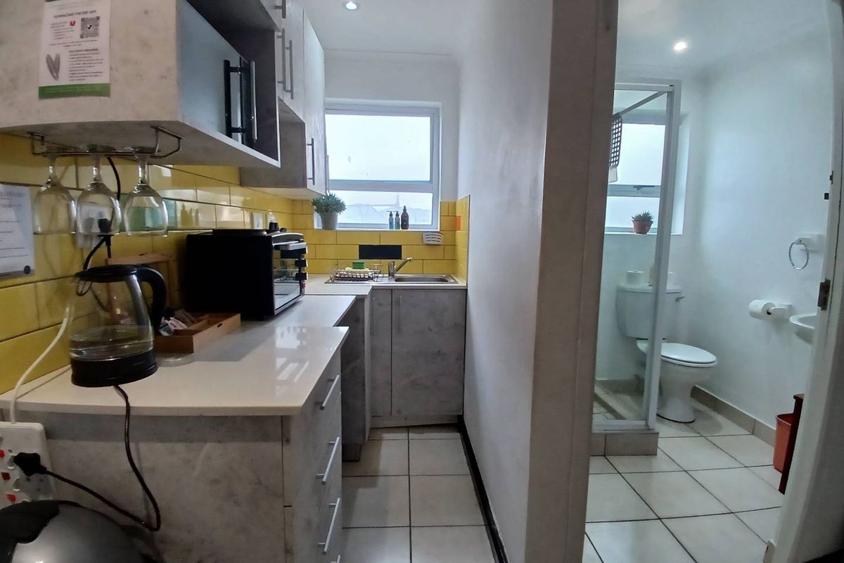 Compact kitchen area featuring modern grey cabinetry and yellow tiled backsplash, adjacent to a small bathroom with a shower and toilet.