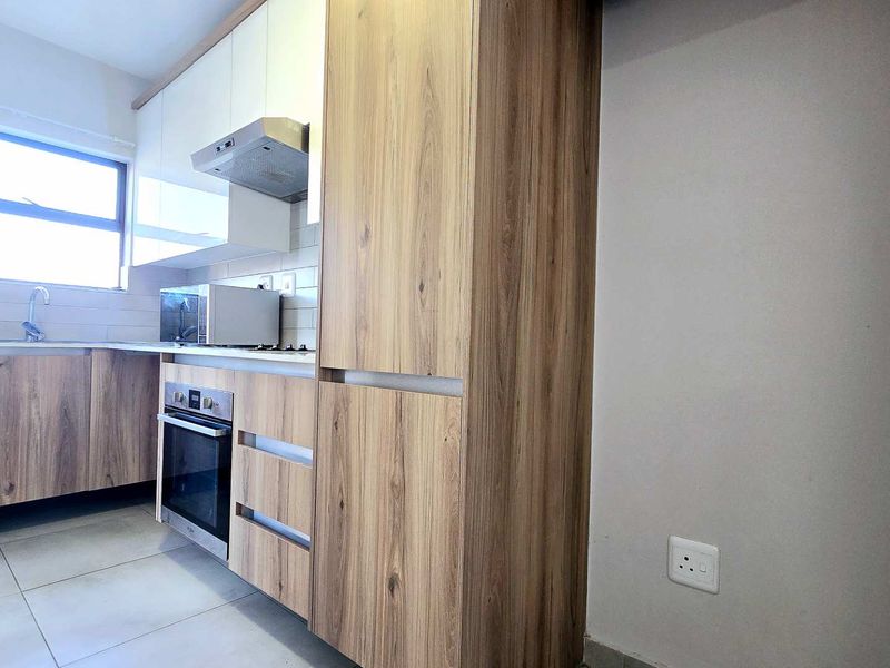 Modern kitchen featuring wood-grain cabinetry, built-in oven and hob, extractor fan, and neutral tiled flooring in a clean, contemporary layout.