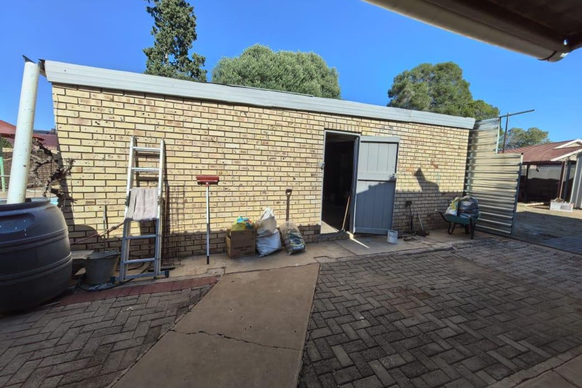 Exterior view of a brick outbuilding or garage featuring a paved courtyard area and a rainwater collection tank.