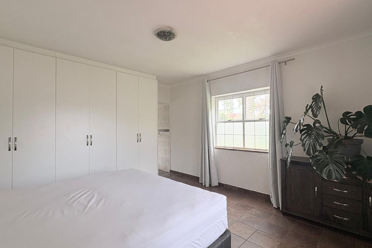 A bedroom featuring built-in cupboards, tiled flooring, and a window with security bars, offering a functional and neutral living space.