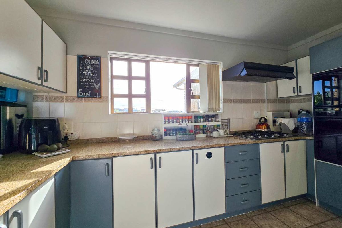 A functional kitchen featuring two-tone cabinetry, granite countertops, a built-in oven, gas hob, and an extractor fan with natural light from the window.