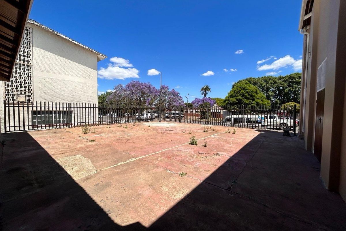 An open paved courtyard area enclosed by metal security fencing, showing signs of wear and requiring surface maintenance.