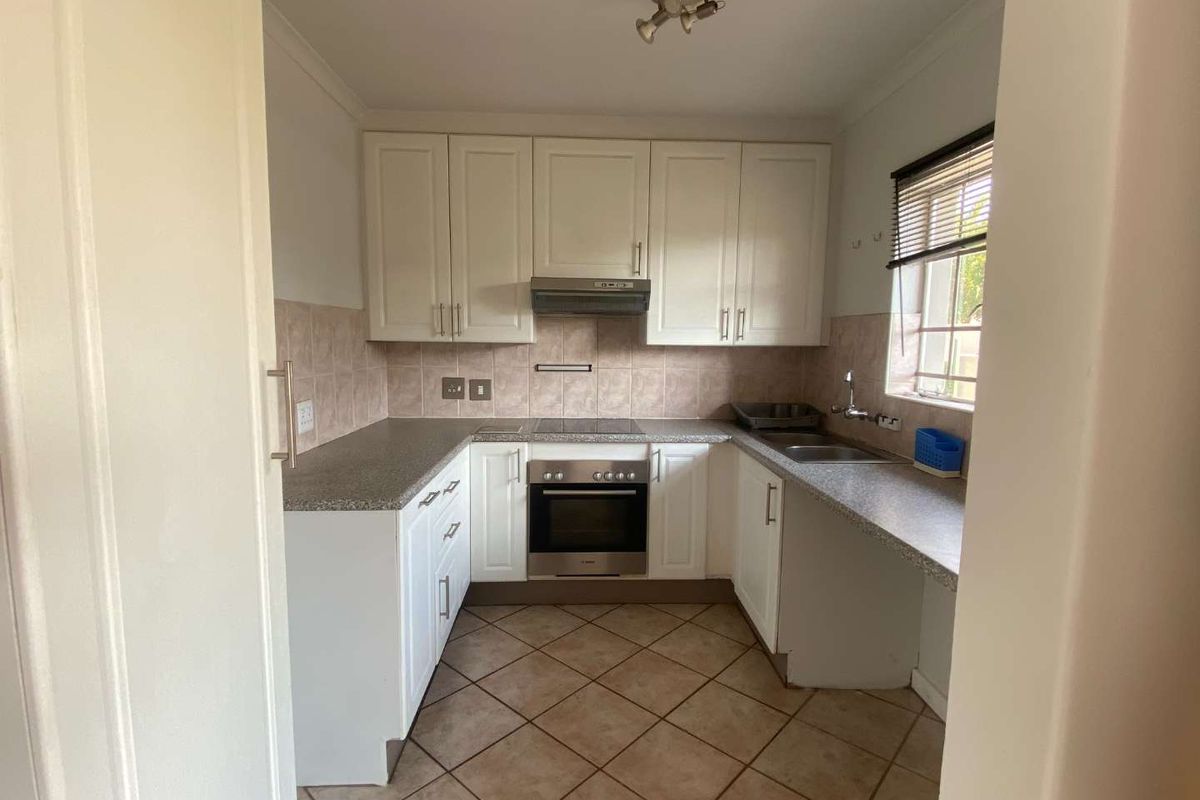 A functional kitchen featuring white cabinetry, laminate countertops, a built-in oven with hob, extractor fan, and tiled flooring.