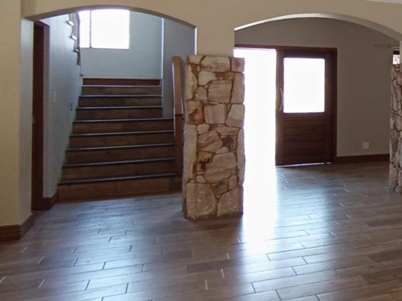 Spacious entrance hall featuring wood-look tile flooring, distinctive stone-clad pillars, and a timber staircase leading to the upper level.