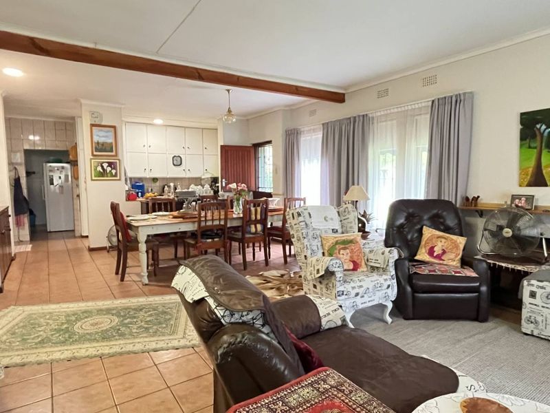 Spacious open-plan living and dining area featuring tiled floors, an exposed timber ceiling beam, and direct access to the garden through sliding glass doors.