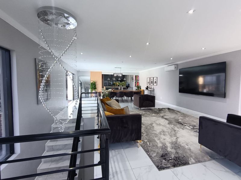 Spacious open-plan living and dining area featuring polished marble flooring, modern recessed lighting, and a sleek staircase with a contemporary crystal chandelier.