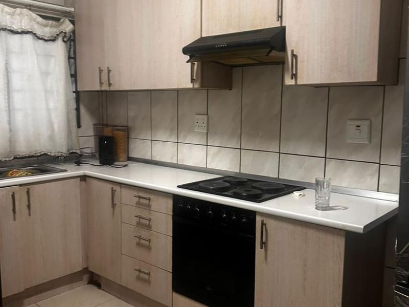 A functional kitchen featuring light wood-tone cabinetry, white countertops, a built-in oven with electric hob, and tiled finishes throughout.