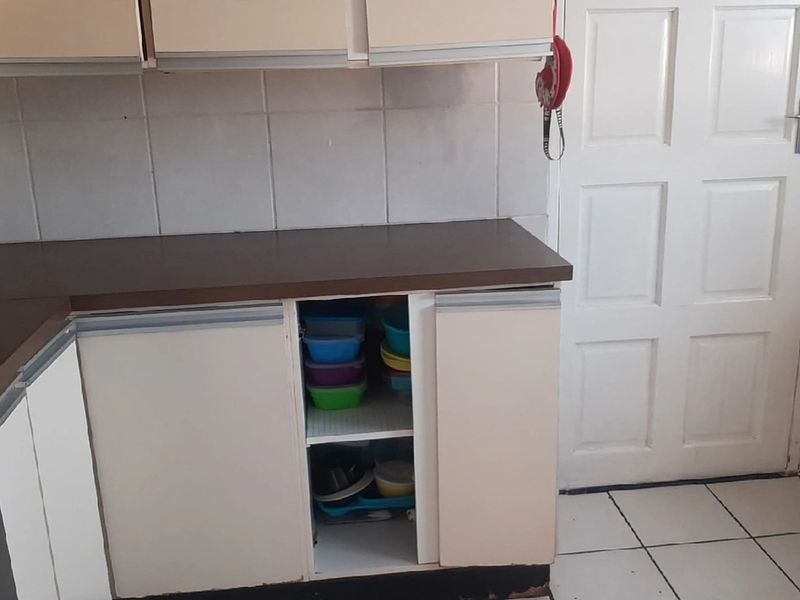 A functional kitchen area featuring laminate countertops, tiled backsplash, and tiled flooring, currently showing signs of wear and missing cabinet hardware.