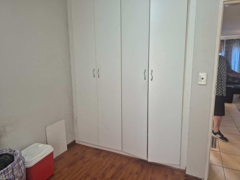 A bedroom featuring built-in cupboards and laminate flooring, currently vacant and in need of cosmetic attention.