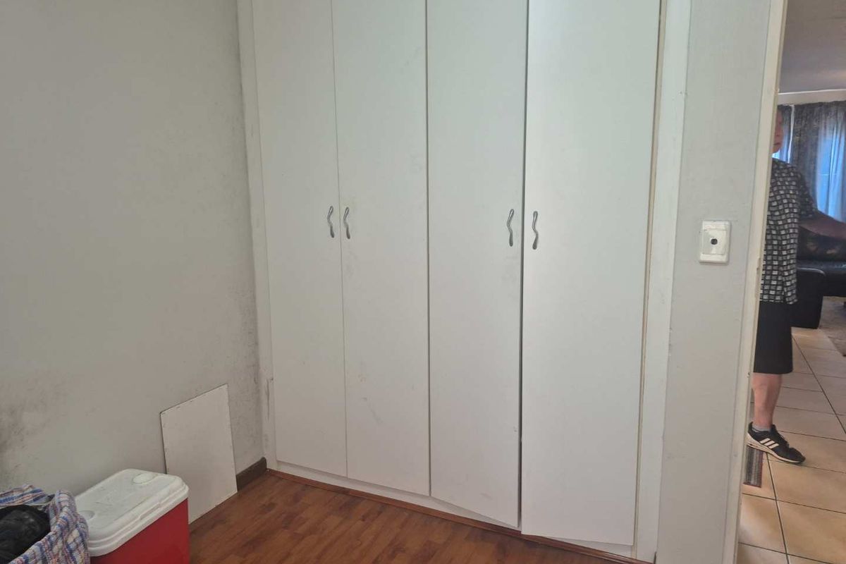 A bedroom featuring built-in cupboards and laminate flooring, currently vacant and in need of cosmetic attention.