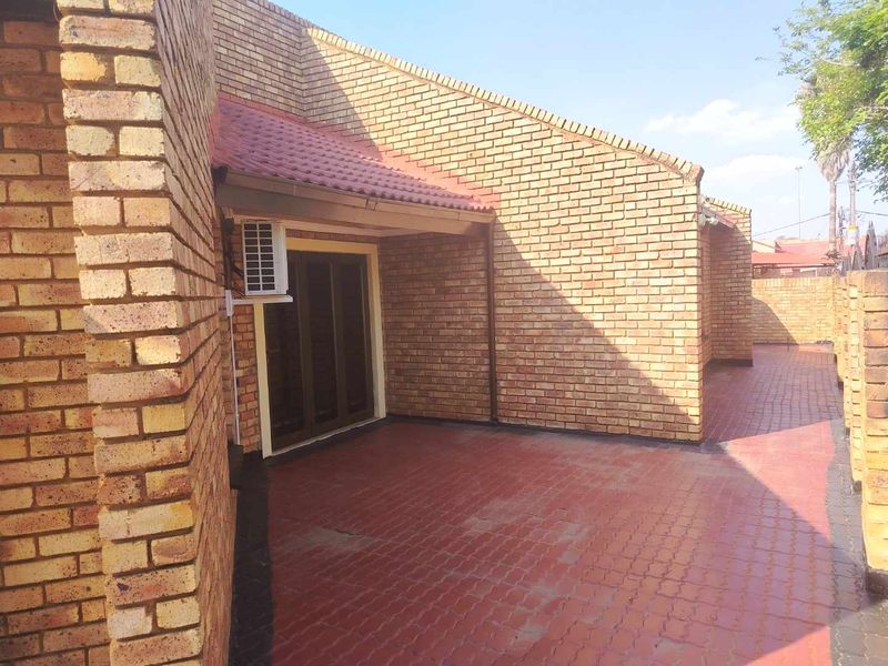 A covered outdoor patio area featuring face brick walls, paved flooring, and a sliding glass door entrance with an integrated air conditioning unit.