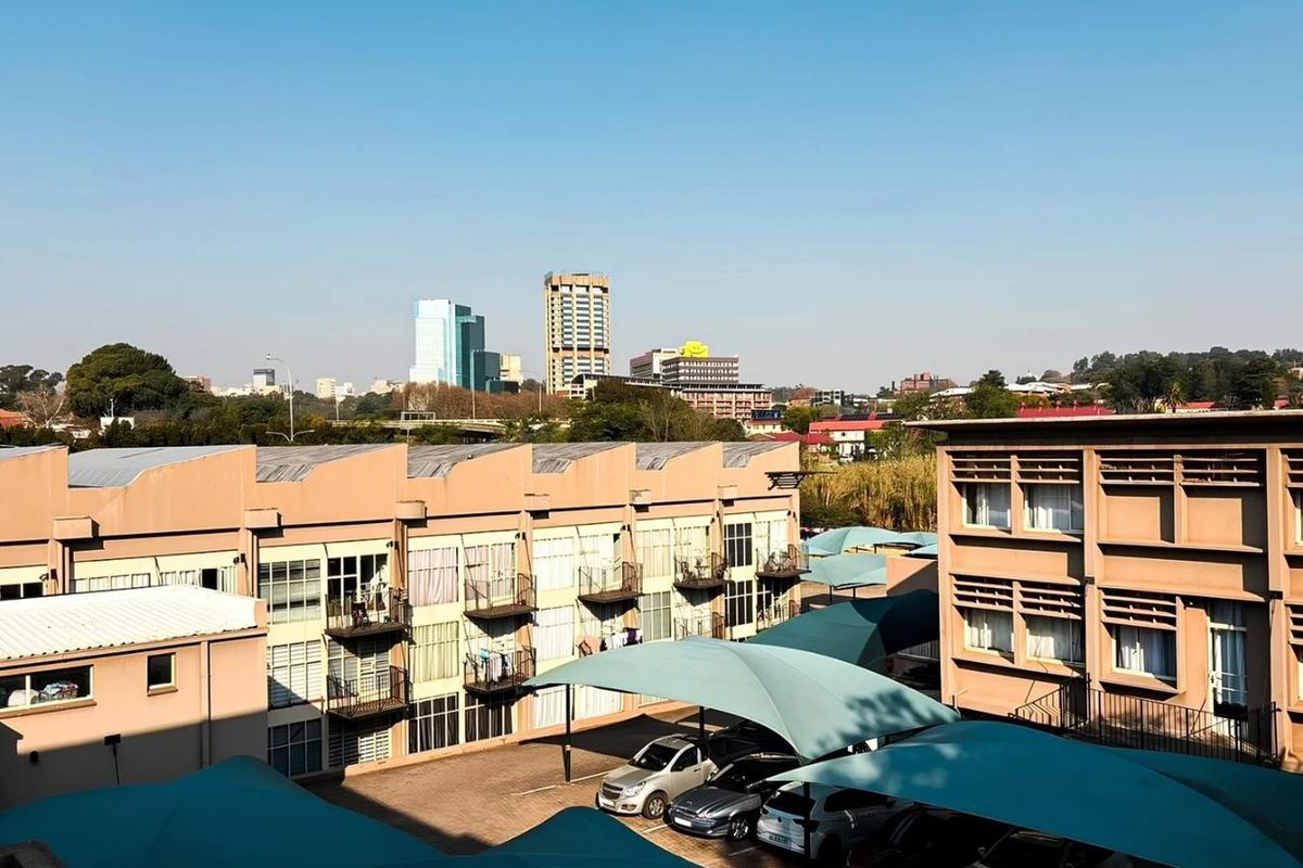 Elevated view of the apartment complex rear courtyard featuring paved parking bays with shade cloth structures and surrounding residential building facades.