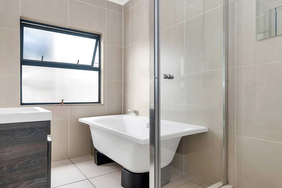 Modern bathroom featuring a freestanding bathtub, a glass-enclosed shower, and neutral wall tiling with a window for natural light.