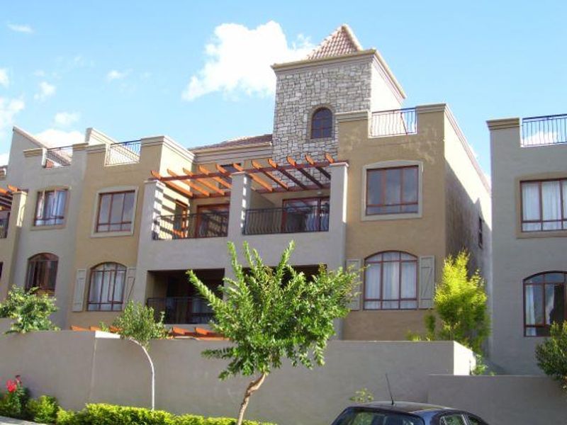 A multi-story apartment building facade featuring stone accents, timber pergolas, wrought iron balcony railings, and arched window detailing.