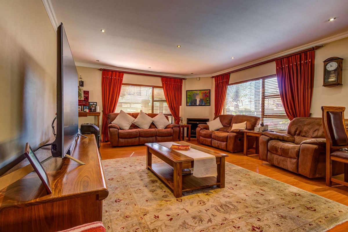 A spacious living room featuring warm timber flooring, recessed downlighting, and large windows with venetian blinds, creating a comfortable and inviting atmosphere.