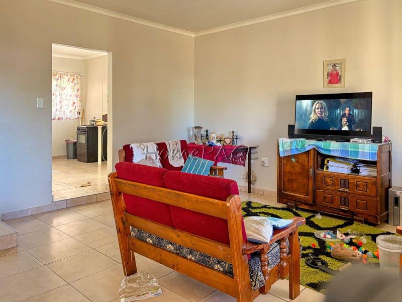 A living room area with tiled flooring and coved ceilings, featuring an open-plan layout that connects to the adjacent kitchen space.