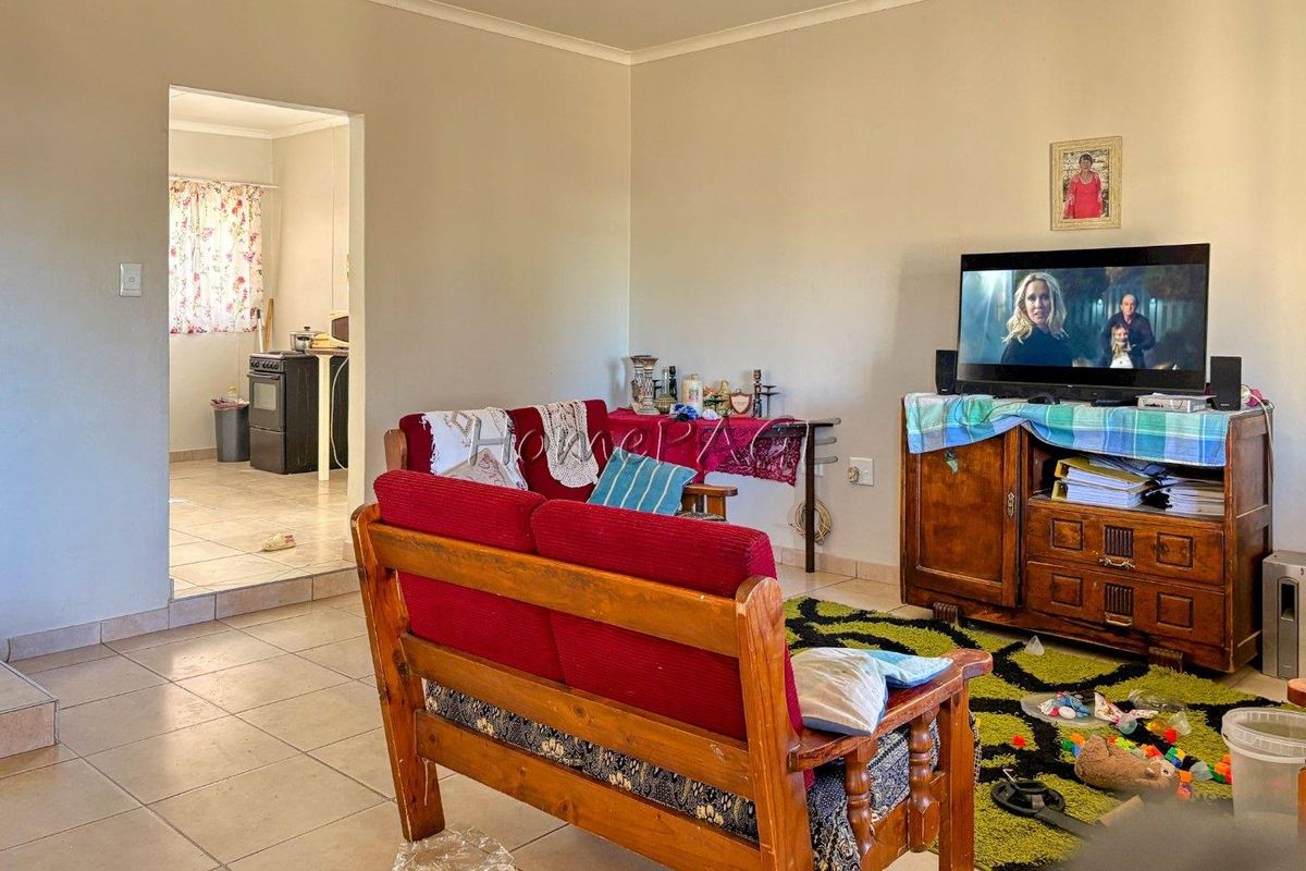 A living room area with tiled flooring and coved ceilings, featuring an open-plan layout that connects to the adjacent kitchen space.