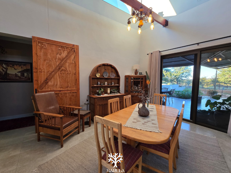 Spacious dining area featuring high vaulted ceilings with exposed timber beams, large sliding glass doors leading to the patio, and tiled flooring.
